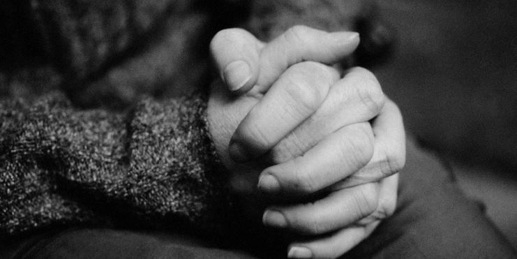 Nahaufnahme von zwei Händen, die ineinander verschränkt sind, vor einem unscharfen Hintergrund.